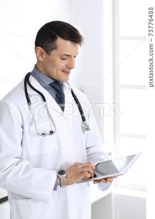 Doctor man using tablet computer for network research or virtual disease treatment. Perfect medical service in clinic. Happy future for modern medicine, medic data and healthcare concepts Doctor man using tablet computer for network research or virtual disease treatment. Perfect medical service in clinic. Happy future for modern medicine, medic data and healthcare concepts 73776488