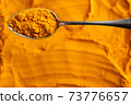Turmeric powder on a spoon above a turmeric background, top view with copy space 73776657