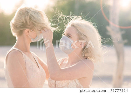 Lesbian couple wedding, wear masks to prevent epidemic COVID-19, on sand background 73777334