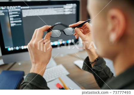 Male IT specialist holds glasses at pc monitor Male IT specialist holds glasses at pc monitor 73777493