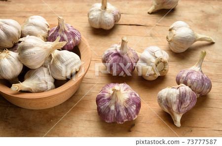 bunch of fresh garlic in a wooden plate on a brown table 73777587