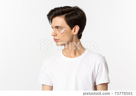 People, lgbtq community and lifestyle concept. Profile view of handsome gay man with glitter on face, looking left, standing over white background 73778501