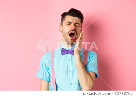 Image of tired guy in bow-tie yawning with opened mouth and closed eyes, standing sleepy, feeling fatigue, standing over pink background 73778703