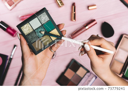 Woman working with green eyeshadow palette on pink flat lay cosmetics collection background. Tools Woman working with green eyeshadow palette on pink flat lay cosmetics collection background. Tools 73779241