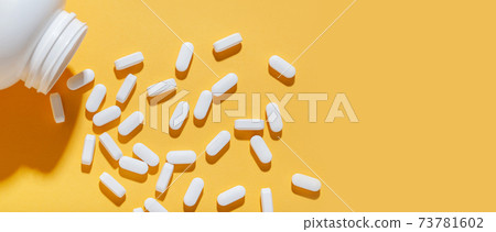 White pills are poured from a jar on a yellow background. Food supplement, multivitamins, medications. 73781602