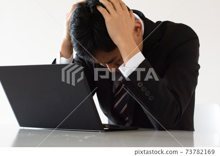 A businessman holding his head in front of a laptop 73782169