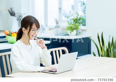 戴著眼鏡在廚房中使用一台筆記本電腦的女人 戴著眼鏡在廚房中使用一台筆記本電腦的女人 73783390