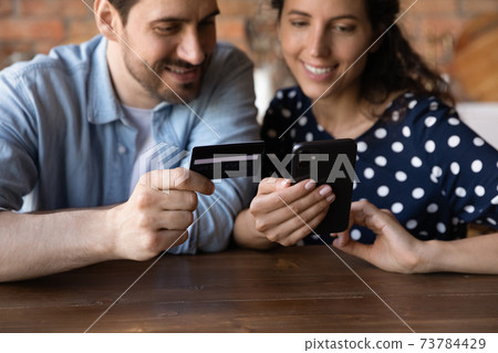 Happy couple shop online on cell with card Happy couple shop online on cell with card 73784429