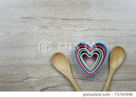 Heart-shaped mold and wooden spoon rests on a wooden table and has a copy space. 73784996