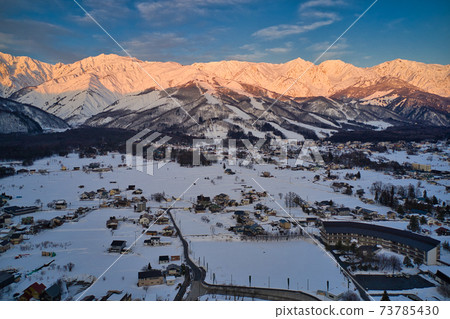 Hakuba Sanzan in the morning glow, the magnificent Happoone ski resort and Hakuba village cityscape Hakuba village, Nagano prefecture (aerial view by drone) 73785430