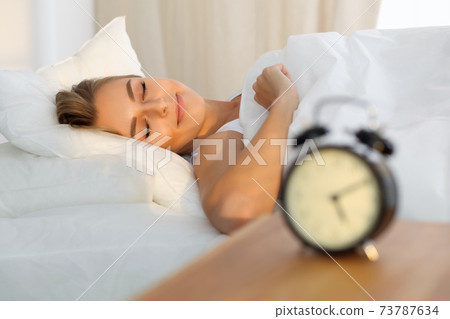 Beautiful young woman sleeping while lying in bed comfortably and blissfully Sunbeam dawn on her face Beautiful young woman sleeping while lying in bed comfortably and blissfully Sunbeam dawn on her face 73787634