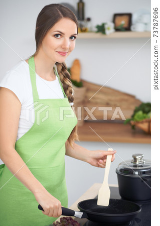 Young woman cooking in a kitchen. Housewife tasting soup by wooden spoon 73787696