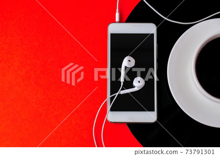 Cup of black coffee on vynil record. Copy space. Listening to music. Retro style. Mobile phone with headphones. Cup of black coffee on vynil record. Copy space. Listening to music. Retro style. Mobile phone with headphones. 73791301