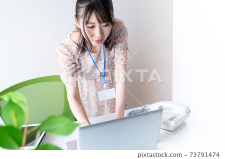 一個穿著電腦的年輕女子站在桌子前同時操作電腦 73791474