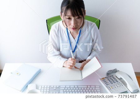 A young woman working on a PC while looking at her notebook A young woman working on a PC while looking at her notebook 73791487