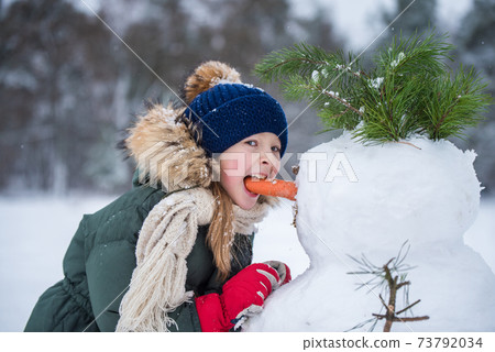Happy girl child plaing with a snowman on a snowy winter walk 73792034