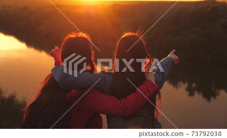 Girls hug at sunset in the sky. Traveling women at sunrise. Tourist trips around the world in the glare of the sun. Spend the weekend with your beloved family in nature. Family life. Teamwork. Close 73792038
