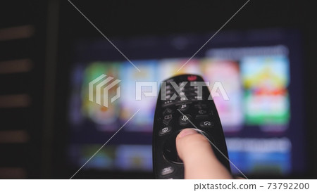 Woman hand selects internet tv channels with remote control, close-up. Person controls TV using a modern remote control. Girl watches smart TV and uses black remote control. Blurry tv scrolls pages Woman hand selects internet tv channels with remote control, close-up. Person controls TV using a modern remote control. Girl watches smart TV and uses black remote control. Blurry tv scrolls pages 73792200