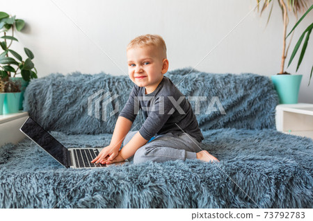 Little baby boy playing on laptop on sofa at home. 73792783