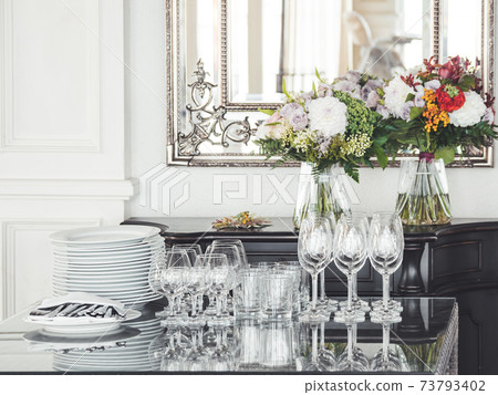 Wine glasses, cutlery, napkins on table. Dishware for banquets and parties. Bouquets of colorful garden flowers and mirror in silver frame. Wine glasses, cutlery, napkins on table. Dishware for banquets and parties. Bouquets of colorful garden flowers and mirror in silver frame. 73793402