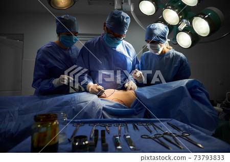 Surgical team standing beside patient in operating room. Surgical team standing beside patient in operating room. 73793833