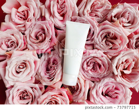 Unbranded white squeeze bottle plastic tube and pink roses background. Bottle for branding and label. Natural organic spa cosmetic. Copy space, Flower flatlay. Mockup, top view. 73797715