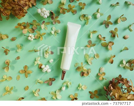 Unbranded face and eye cream squeeze cosmetic tube with long nozzle and bronze screw cap and dried hydrangea flowers on green background. Natural organic spa cosmetics. Top view, mockup 73797717