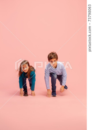 Happy children isolated on coral pink studio background. Look happy, cheerful, sincere. Copyspace. Childhood, education, emotions concept 73798063