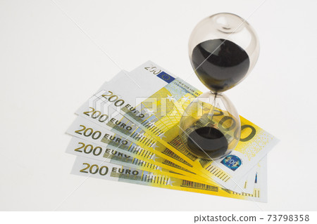 Concept or conceptual euro paper money banknote with a sand glass or time background. Concept or conceptual euro paper money banknote with a sand glass or time background. 73798358