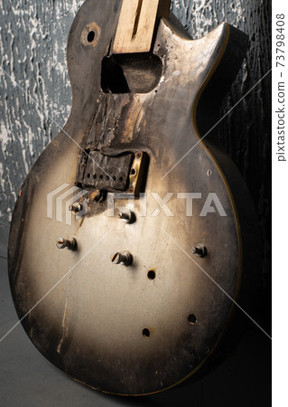 Burnt broken old electric guitar against the background of a dark wall Burnt broken old electric guitar against the background of a dark wall 73798408