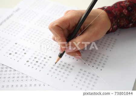 Female hand holds pencil and marks answers to test Female hand holds pencil and marks answers to test 73801844