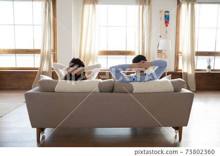 Rear view young couple relaxing on couch in modern apartment Rear view young couple relaxing on couch in modern apartment 73802360