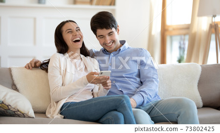 Happy young couple using phone, laughing, having fun together Happy young couple using phone, laughing, having fun together 73802425