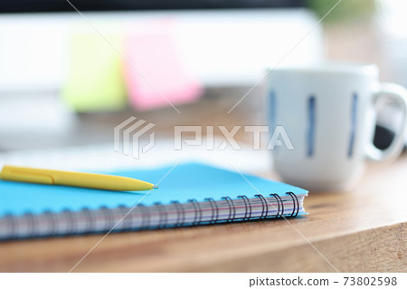 On table is cup next to pen and diary for notes 73802598