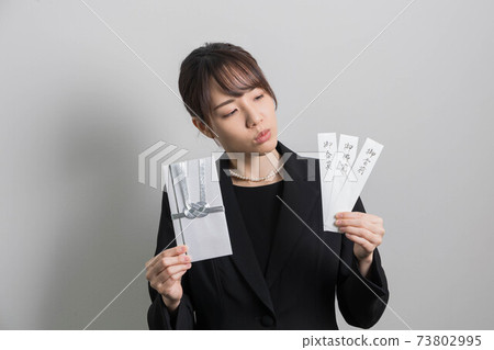 一個年輕女子，穿著哀悼服，拿著一個非祝賀的袋子[葬禮] 73802995