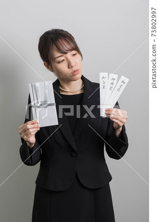 一個年輕女子，穿著哀悼服，拿著一個非祝賀的袋子[葬禮] 73802997