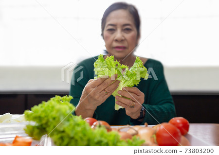 Senior woman prepare green salad from lettuce and tomato. Senior woman prepare green salad from lettuce and tomato. 73803200