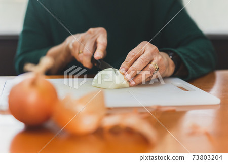 Senior woman hands cut onions with a knife. Senior woman hands cut onions with a knife. 73803204