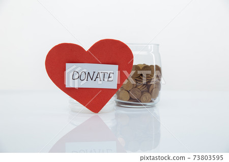 Red heart with DONATE word near glass ban with coins close-up. Charity and donation concept. Red heart with DONATE word near glass ban with coins close-up. Charity and donation concept. 73803595