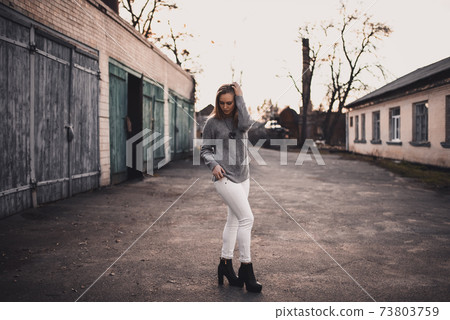 Woman in White pants gray knitted sweater black boots on gray wooden gates Woman in White pants gray knitted sweater black boots on gray wooden gates 73803759