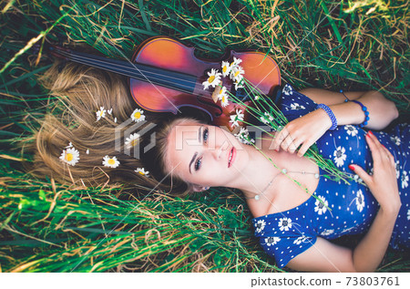 Young girl blonde lies in grass with violin. Young girl blonde lies in grass with violin. 73803761