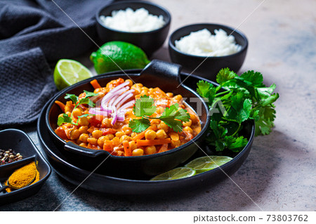 Vegan chickpea curry with rice and cilantro in black plate, dark background. Indian cuisine concept. Vegan chickpea curry with rice and cilantro in black plate, dark background. Indian cuisine concept. 73803762