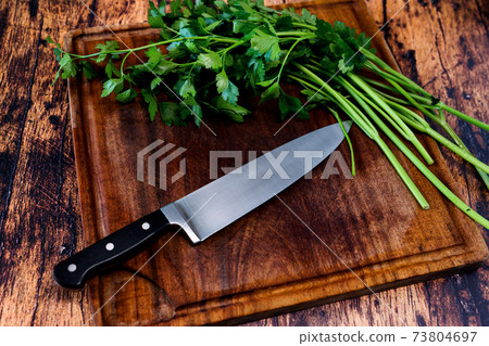 Worn wooden cutting board on an old worn wooden table with a knife on it and parsley 73804697