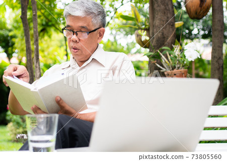 senior old man reading a book in the park and drinking water. Concept of retirement lifestyle and hobby. 73805560