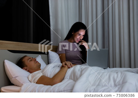 Woman sitting on bed in the night and using laptop computer Woman sitting on bed in the night and using laptop computer 73806386