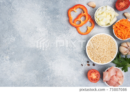 Raw ingredients for cooking pilaf, Brown rice and chicken fillet, grated carrots and chopped onions, pepper tomato garlic herbs and spices. Gray background, top view. copy space Raw ingredients for cooking pilaf, Brown rice and chicken fillet, grated carrots and chopped onions, pepper tomato garlic herbs and spices. Gray background, top view. copy space 73807086
