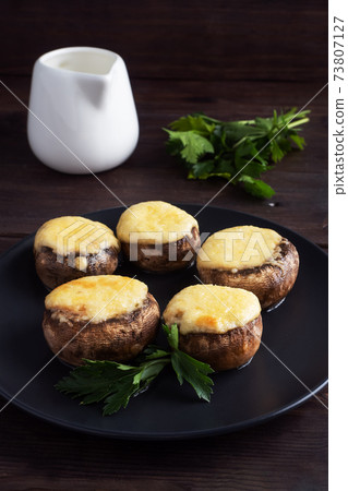 Baked mushrooms stuffed with cheese and herbs on a black plate. wooden background. Baked mushrooms stuffed with cheese and herbs on a black plate. wooden background. 73807127