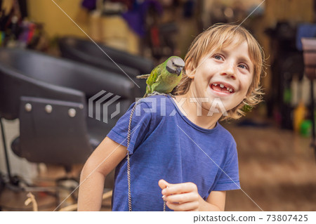 Kid playing with his pet green parrot 73807425