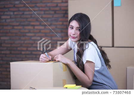 Businesswoman taping up a cardboard box, Asian woman packing boxes among stack of parcels in her shopping online business at home 73807468