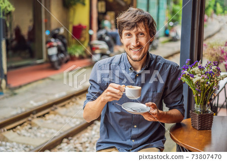 Young man traveler drinks Vietnamese coffee with egg sitting by the railway paths which go through residential area in Hanoi city. Hanoi Train Street is a famous tourist destination. Vietnam reopens Young man traveler drinks Vietnamese coffee with egg sitting by the railway paths which go through residential area in Hanoi city. Hanoi Train Street is a famous tourist destination. Vietnam reopens 73807470